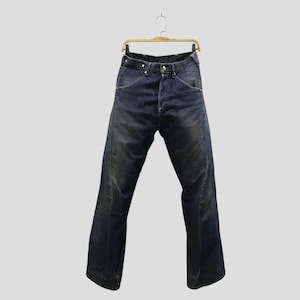 May include: Dark blue denim jeans featuring a high-waisted design with a button fly closure, prominent curved seam detailing along the hips, and a wide-leg silhouette. The fabric displays a subtle faded wash effect throughout the legs.