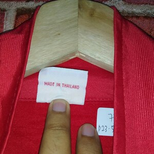 Puede incluir: Primer plano de una camisa roja con una etiqueta blanca que dice "Made in Thailand".