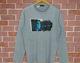 May include: A grey long-sleeved t-shirt featuring a colourful graphic print of Andy Warhol's portrait and his signature.