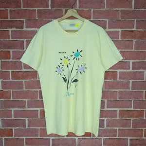 Może przedstawiać: Jasnożółta koszulka z nadrukiem kwiatowym i tekstem "Microsoft" i "Mom" z przodu.