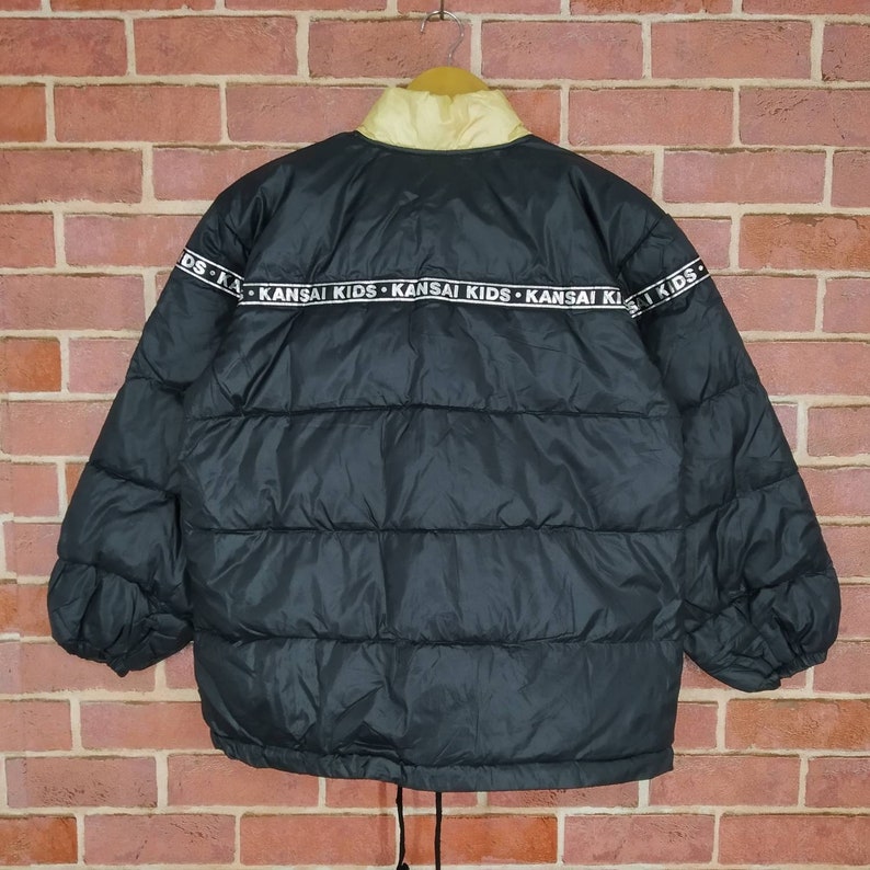 May include: Black puffer jacket with a yellow lining and a white band around the bottom with the text "KANSAI KIDS" repeated.