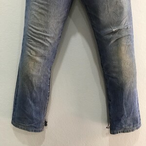 May include: Faded blue denim jeans with a distressed look. The jeans have a worn appearance with light discoloration and a small tear on the right knee. The bottom hems are slightly frayed.