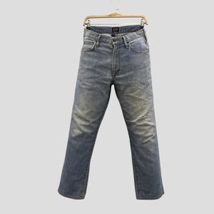 May include: Light blue denim jeans hanging on a wooden hanger. The jeans have a classic five-pocket design, a button and zipper closure, and a faded wash. The jeans are a straight-leg style.