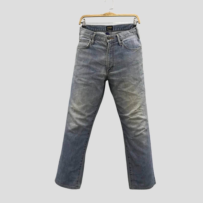 May include: Light blue denim jeans hanging on a wooden hanger. The jeans have a classic five-pocket design, a button and zipper closure, and a faded wash. The jeans are a straight-leg style.
