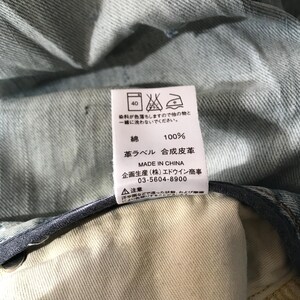 K&ouml;nnte beinhalten: Nahaufnahme eines wei&szlig;en Etiketts mit japanischem Text und Pflegehinweisen, das an hellblauem Denim-Stoff befestigt ist. Das Etikett gibt an, dass das Kleidungsst&uuml;ck aus 100 % Baumwolle besteht und in China hergestellt wurde.
