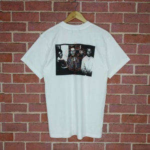 May include: White t-shirt with a black and white band photo print on the back. The photo shows four people with a red geometric design overlayed on the image.