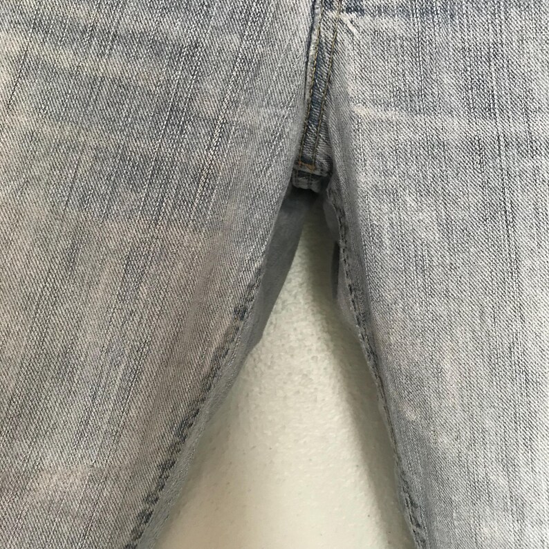 K&ouml;nnte beinhalten: Nahaufnahme einer hellblauen Jeans. Die Jeans zeigt die Vorderseite der Hose mit der Naht und dem Bereich, in dem sich der Rei&szlig;verschluss befinden w&uuml;rde. Der Denim hat ein verwaschenes, abgenutztes Aussehen.