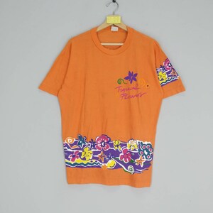 Puede incluir: Camiseta naranja de manga corta con estampado floral colorido y el texto "Tropical Flowers" en la parte delantera.