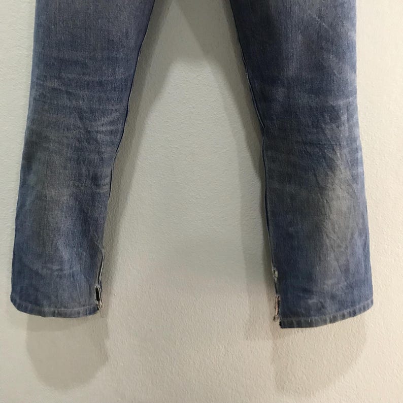May include: Faded blue denim jeans with a straight leg cut. The jeans have a worn appearance with visible fading and distressing. The bottom hems feature small slits. The jeans are a classic style.