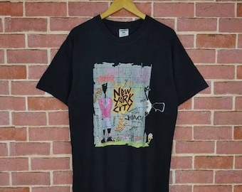 May include: Black t-shirt with a graphic print of a cartoon figure in front of a brick wall with the text "New York City" and "JillAC".