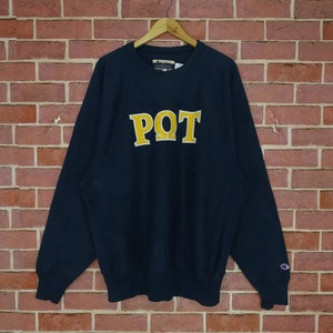 Puede incluir: Una sudadera Champion azul marino con un logotipo "PQT" bordado en amarillo en la parte delantera.