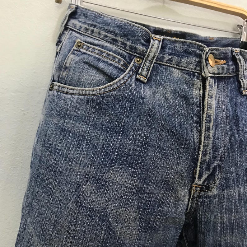 Op de afbeelding: Close-up van een blauwe spijkerbroek. De jeans heeft een klassiek ontwerp met vijf zakken, een knoopsluiting en een ritssluiting. De denim heeft een vervaagde, versleten uitstraling.