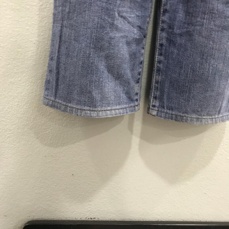 May include: Close-up of the bottom of a pair of light blue denim jeans. The jeans have a slight flare at the hem and show signs of wear. The fabric is a medium wash denim.