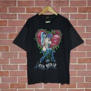May include: Black t-shirt with a graphic print of a woman in a heart-shaped frame with roses and the text "little whip".