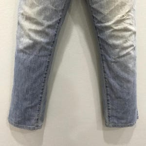 May include: Light blue denim jeans with a faded wash effect. The jeans have a straight leg cut and visible stitching along the seams. The denim has a worn appearance, with lighter areas at the thighs and knees.