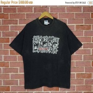 May include: Black t-shirt with a white graphic print of the band No Doubt. The graphic features the band members' faces in a collage style with the band's name written in a stylized font.