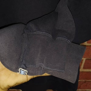 May include: Black sweatshirt with a blue embroidered logo on the cuff. The sweatshirt is made of a soft, comfortable fabric.