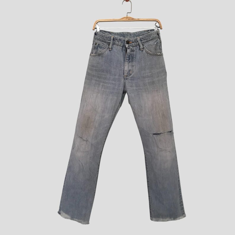 K&ouml;nnte beinhalten: Hellblaue Jeans aus Denim mit Used-Look und einem Riss am rechten Knie. Die Jeans h&auml;ngen an einem Holzb&uuml;gel. Die Jeans haben ein klassisches F&uuml;nf-Taschen-Design.