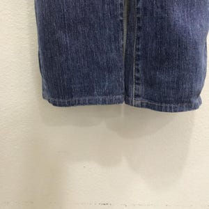 Op de afbeelding: Close-up van de zoom van een blauwe denim jeans. De jeans heeft een klassiek vijf-zakken ontwerp en een rechte pijp. De denim heeft een medium wassing met subtiele vervaging en slijtage.