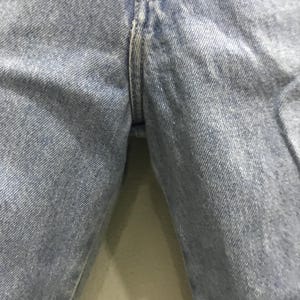 May include: Close-up of light blue denim jeans. The image focuses on the seam and the fabric's texture. The denim appears to be well-worn, with subtle variations in color.