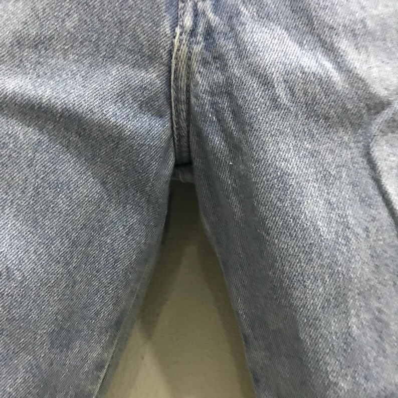 May include: Close-up of light blue denim jeans. The image focuses on the seam and the fabric's texture. The denim appears to be well-worn, with subtle variations in color.