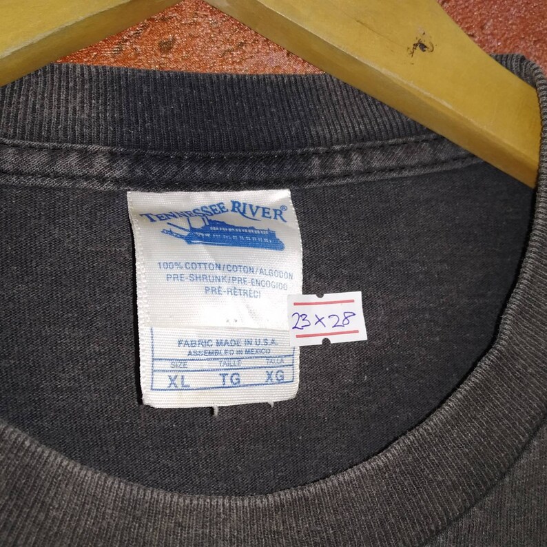 May include: A black t-shirt with a white tag that says "Tennessee River" and has a boat graphic. The tag also says "100% Cotton/Coton/Algodon", "Pre-Shrunk/Pre-Encogido", "Pre-Retreci", "Fabric Made in U.S.A.", "Assembled in Mexico", "Size XL", "Talle TG", "Talla XG".