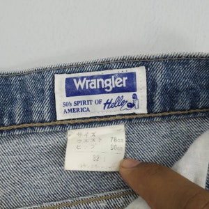 Może przedstawiać: Zbliżenie niebieskich dżins&oacute;w z metką Wrangler. Na metce widnieje napis "Wrangler 50's Spirit of America Hello". Dżinsy mają metkę z rozmiarem z wymiarami w centymetrach. Talia ma 78 cm, a biodra 98 cm.