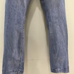 May include: A pair of blue denim jeans featuring a straight-leg cut with visible vertical seams running down the front of each leg. The denim has a medium-wash finish with subtle fading throughout the fabric and a horizontal hem at the bottom.
