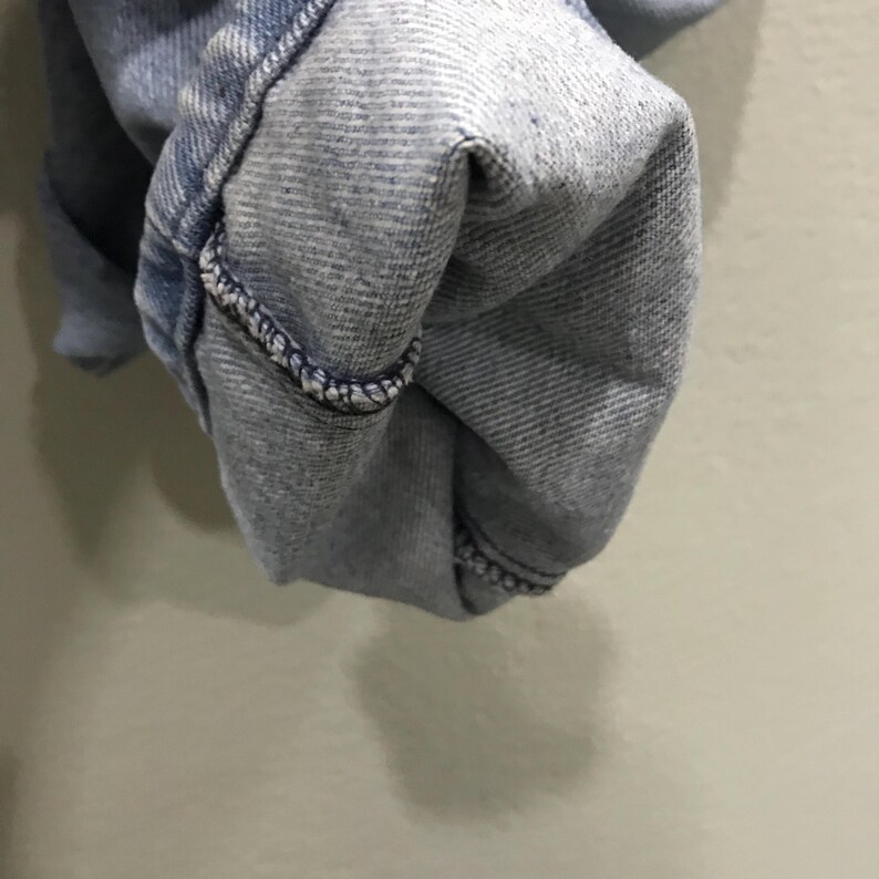 May include: Close-up of light blue denim fabric, showing the folded hem of a pair of jeans. The hem is turned up, revealing the inside of the denim. The stitching is visible along the edge of the fold.