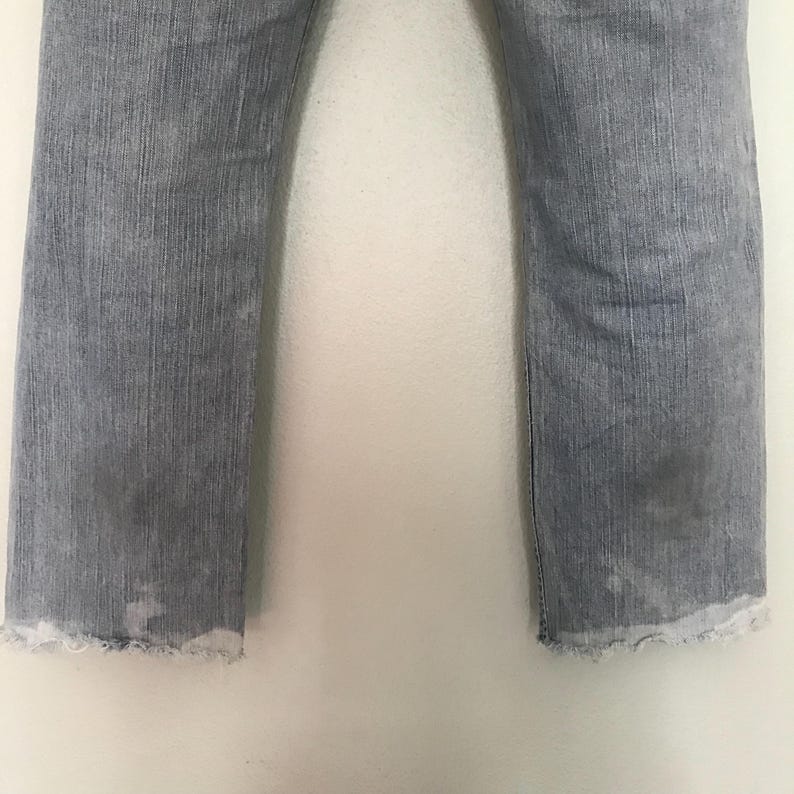 K&ouml;nnte beinhalten: Hellblaue Jeans mit ausgefranstem Saum. Die Jeans haben einen geraden Beinverlauf und weisen Gebrauchsspuren mit Verf&auml;rbungen auf. Das Bild zeigt eine Nahaufnahme des unteren Teils der Jeans.