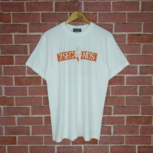 May include: White t-shirt with an orange graphic of a screaming face and the text "7 SECONDS" on the front.