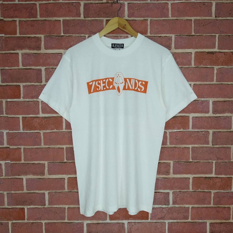 May include: White t-shirt with an orange graphic of a screaming face and the text "7 SECONDS" on the front.