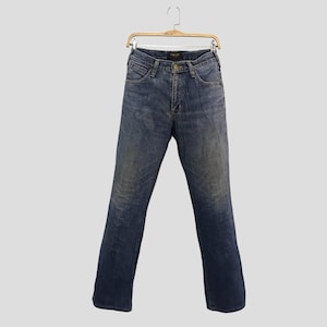 Op de afbeelding: Blauwe denim jeans hangend aan een houten hanger. De jeans hebben een klassiek ontwerp met vijf zakken, een knoop- en ritssluiting en een vervaagde wassing. De jeans hebben een rechte pijp en lijken van een medium gewicht denim te zijn.
