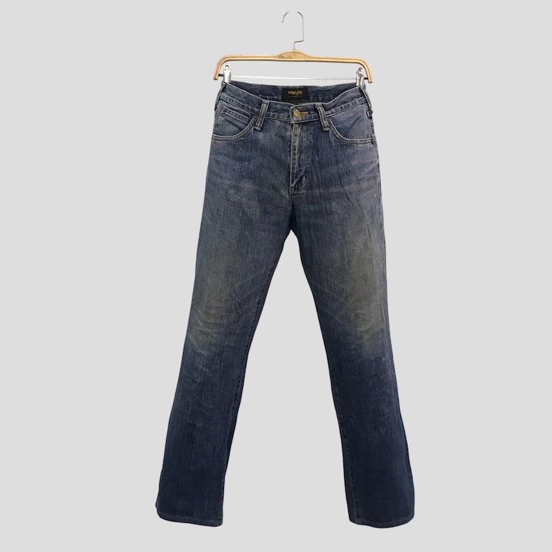 Op de afbeelding: Blauwe denim jeans hangend aan een houten hanger. De jeans hebben een klassiek ontwerp met vijf zakken, een knoop- en ritssluiting en een vervaagde wassing. De jeans hebben een rechte pijp en lijken van een medium gewicht denim te zijn.