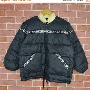 May include: Black puffer jacket with a white fleece lining and a zipper closure. The jacket has a band around the waist and the sleeves with the text "KANSAI KIDS" repeated.