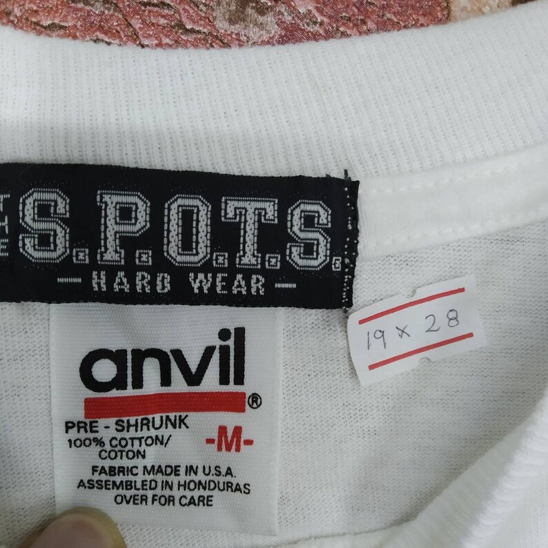 May include: White t-shirt with a black tag that says "S.P.O.T.S. -HARD WEAR-" and a white tag that says "anvil" with the text "PRE-SHRUNK 100% COTTON/COTON -M- FABRIC MADE IN U.S.A. ASSEMBLED IN HONDURAS OVER FOR CARE" and a white tag with the text "19 x 28".