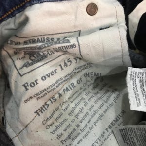 May include: Close-up of the inside of a pair of blue denim jeans. The interior lining features printed text, including "Levi Strauss & Co." and "For over 145 years." A copper-colored button is visible near the top.