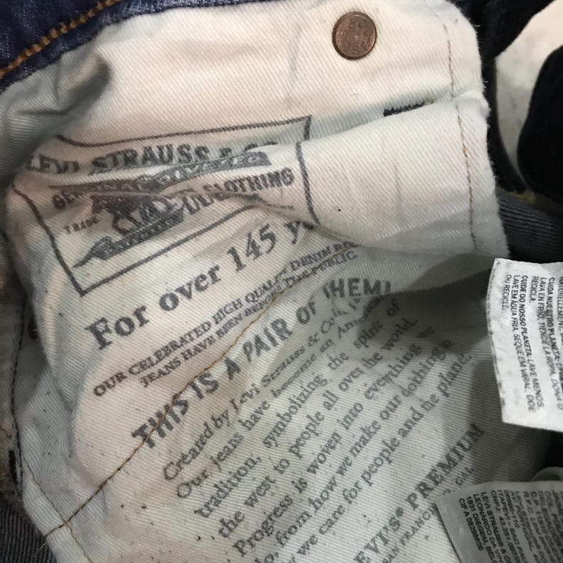 May include: Close-up of the inside of a pair of blue denim jeans. The interior lining features printed text, including "Levi Strauss & Co." and "For over 145 years." A copper-colored button is visible near the top.