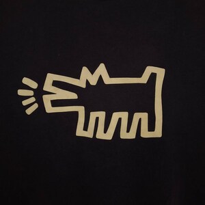 May include: A black t-shirt with a white outline of a dog barking. The dog is stylized with simple lines and a rounded shape.