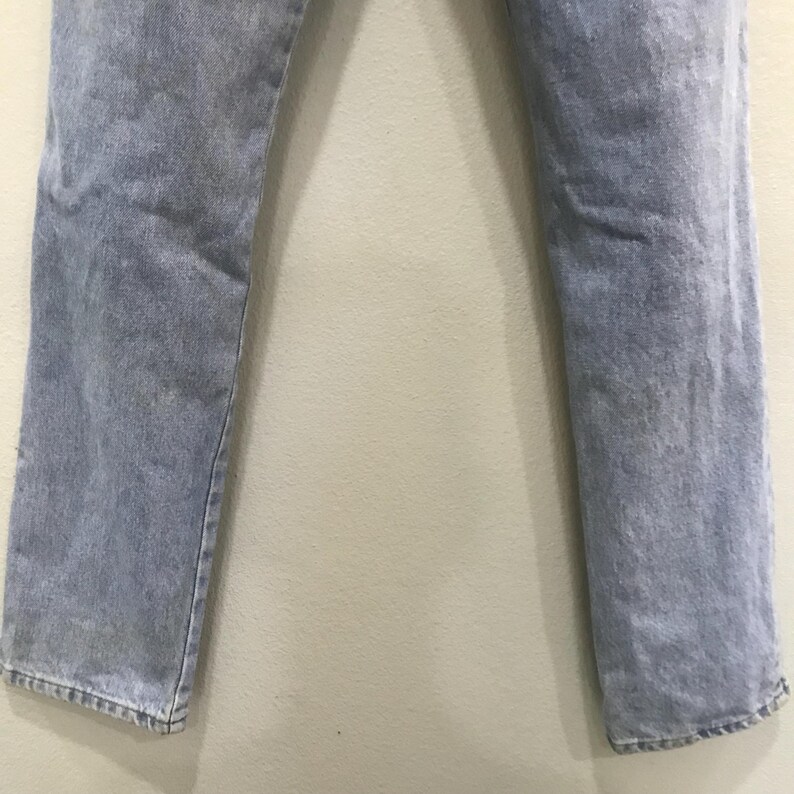 May include: Light blue denim jeans. The jeans have a straight leg cut and a faded appearance. The fabric appears to be a medium weight denim. The jeans are shown from the waist down.