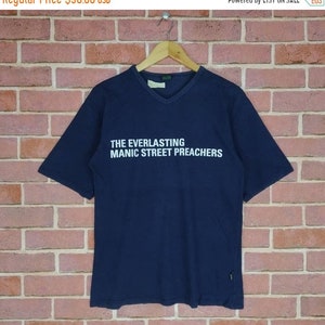 May include: A navy blue short-sleeved t-shirt with a v-neck collar. The shirt has a white print that reads "THE EVERLASTING MANIC STREET PREACHERS".
