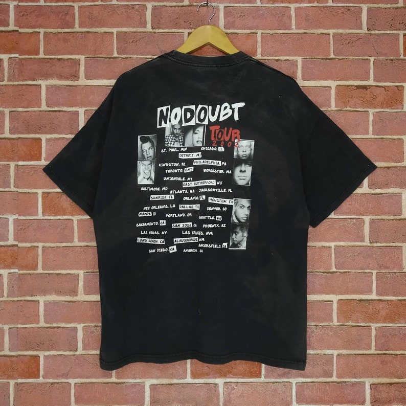 May include: Black t-shirt with a white graphic of the band No Doubt's 2002 tour dates and band member photos. The text "No Doubt Tour 2002" is printed in red.