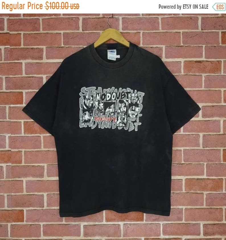 May include: Black t-shirt with a graphic print of the band No Doubt. The print features the band members' faces in a collage style with the words "No Doubt" and "Rock Steady" in the center.
