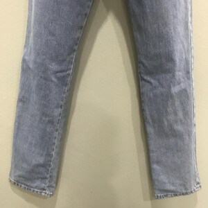 May include: Light blue denim jeans. The jeans have a straight leg cut and a faded appearance. The fabric shows subtle wear patterns, and the hems are slightly frayed. The jeans are displayed against a neutral background.