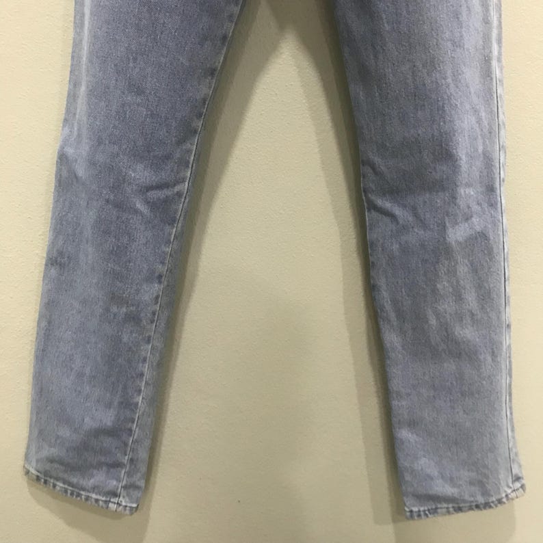 May include: Light blue denim jeans. The jeans have a straight leg cut and a faded appearance. The fabric shows subtle wear patterns, and the hems are slightly frayed. The jeans are displayed against a neutral background.