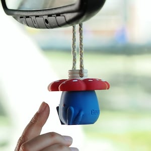 Könnte beinhalten: Ein blau-rotes hängendes Auto-Ornament in Form einer Kreatur mit pilzartigem Hut und weißen Punkten. Das Ornament ist an einer geflochtenen Kordel am Rückspiegel befestigt und zeigt den Teiltext "Gee" an der Seite des Körpers.