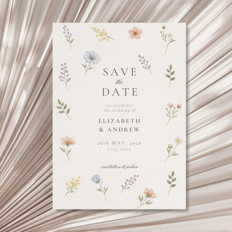 May include: A rectangular wedding save the date card on textured off-white paper featuring watercolor illustrations of small wildflowers in blue, yellow, pink, and green. The text reads: SAVE THE DATE to celebrate the wedding of ELIZABETH & ANDREW 26th MAY, 2026 City, State invitation to follow.