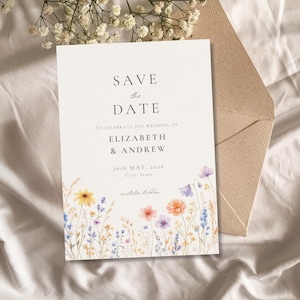 Può includere: Un invito di nozze con il testo "SAVE the DATE" e i nomi Elizabeth & Andrew. L'invito è decorato con fiori ad acquerello nei toni del giallo, arancione, rosa e viola. Sullo sfondo è visibile una busta.