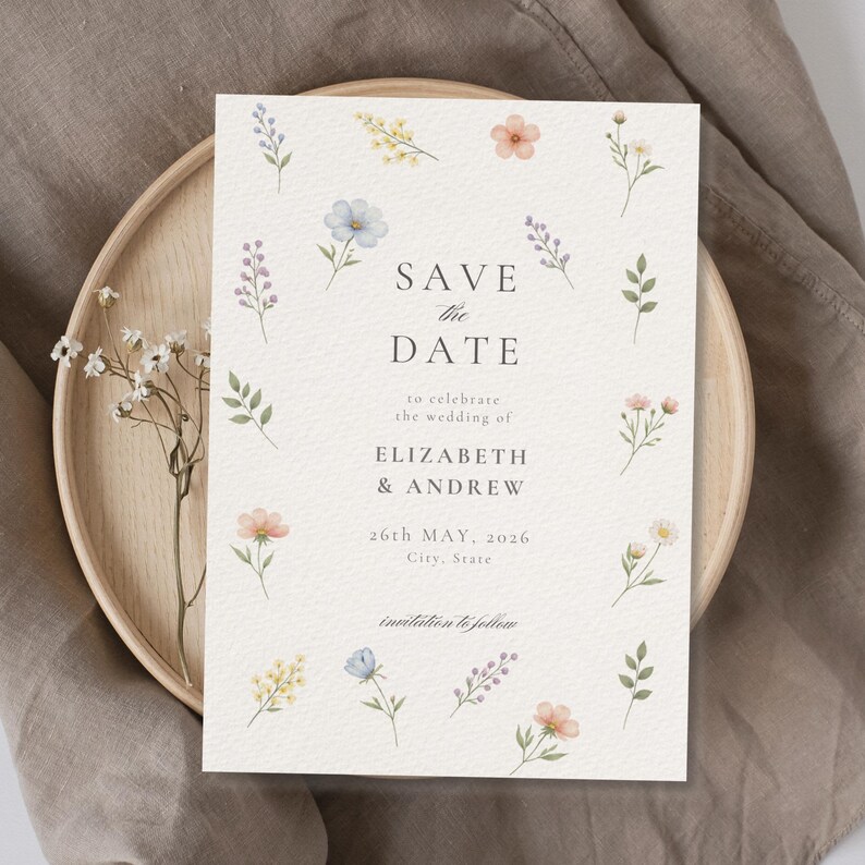 May include: A rectangular Save the Date card featuring a cream-colored textured background with watercolor illustrations of various small wildflowers in shades of blue, yellow, pink, and green, with black text reading Save the Date, Elizabeth & Andrew.