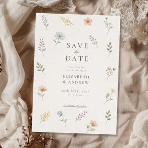 May include: A rectangular white card featuring the text SAVE THE DATE to celebrate the wedding of ELIZABETH & ANDREW 26TH MAY, 2026 City, State invitation to follow, decorated with a border of small watercolor flowers in blue, yellow, and pink.